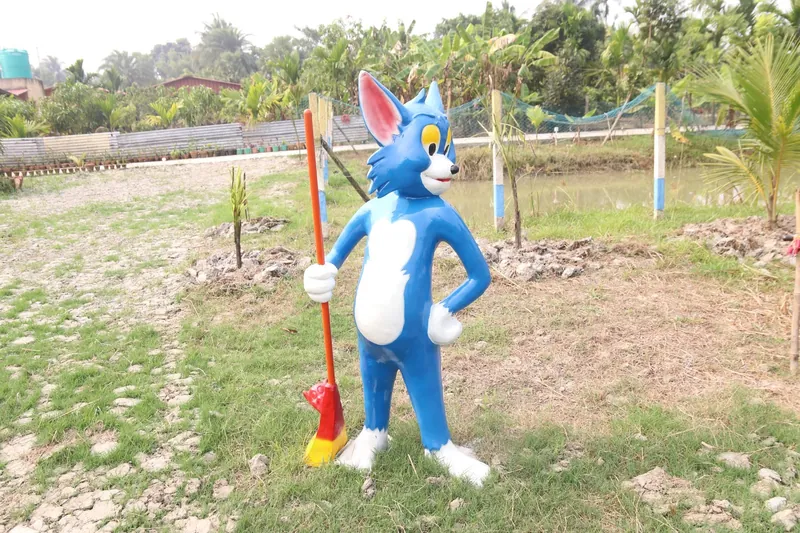 A blue cartoon cat statue holding a broom on the lawn near the pond