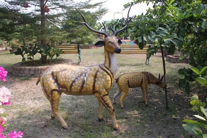 Two spotted deer statues standing on the lawn beside flowering bougainvillea and garden benches