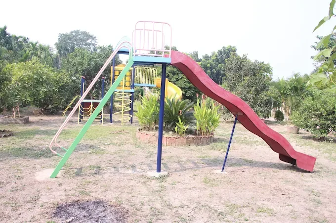 A long red slide attached to a climbing frame on the lawn, with a yellow spiral slide behind